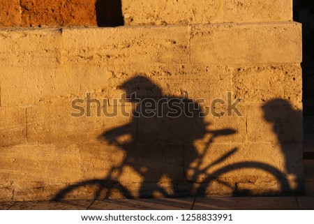 Close up outdoor view of the shadow of a cyclist projected on an ancient stone wall. Silhouette of a person cycling drawn on a textured lighted surface. Bicycle on an urban facade in a french city. 