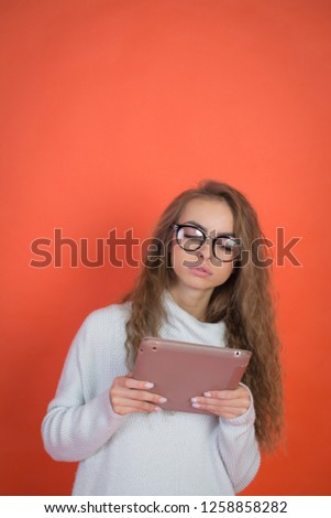 Pretty young woman holding and uses tablet on red background