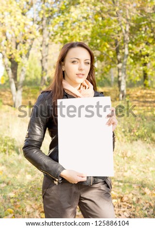 Beautiful trendy young woman holding a blank sign for your text in her hands standing outdoors in woodland