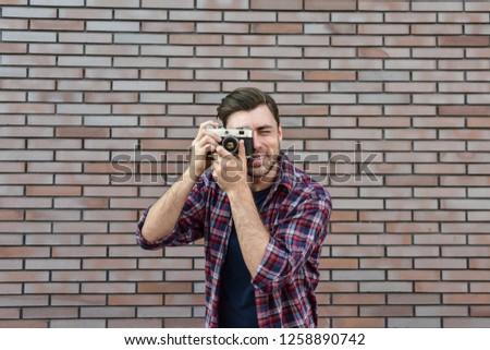 Man with retro photo camera Fashion Travel Lifestyle outdoor while standing against brick wall background.