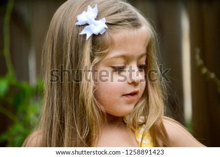 Beautiful little girl in a yellow sundress with her long hair tied back with a white bow. Outdoor horizontal view.