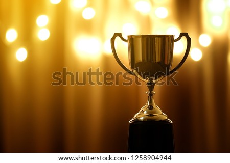 Gold Trophy competition in the dark on the abstract blurred light background with copy space, Spectacular success Concept Royalty-Free Stock Photo #1258904944