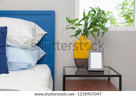 Blue bedding bedroom interior with green plant vase and small picture frame.