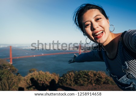 Selfie girl on San Francisco Golden bridge travel. Asian woman adult taking picture with her smartphone during summer vacation hand showing the famous American attraction California USA.