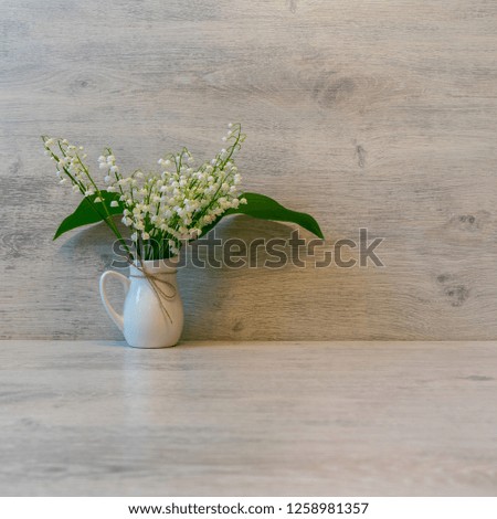 Bouquet of fresh lilies of the valley flowers in small jug on light wooden background. Beautiful spring still life, mock up for greeting card, copy space
