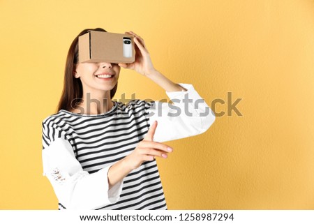 Young woman using cardboard virtual reality headset on color background. Space for text