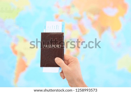 Man holding passport with ticket against blurred map in travel agency, closeup