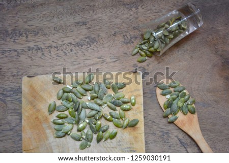 Bowl with pumpkin seeds and a wooden spoon on a wooden table.