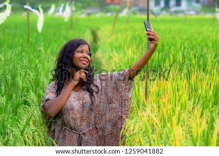 young happy and beautiful black afro American woman in stylish dress posing cool taking selfie photo with mobile phone smiling cheerful at rice field enjoying tropical holidays in exotic village