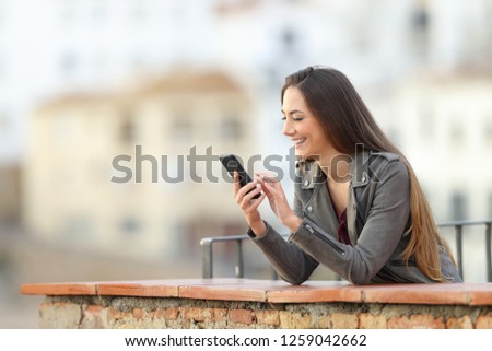 Happy girl using a smart phone in a balcony in a town on vacation