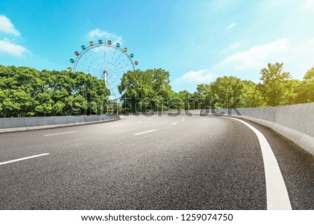 Asphalt road and ferris wheel with green forest landscape