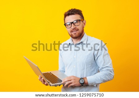 A cheerful young man hold his lapotop over yellow background