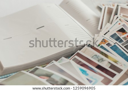 Pile of printed photographs in disorder on a white background near a photoalbum. Picture of the baby on the top.