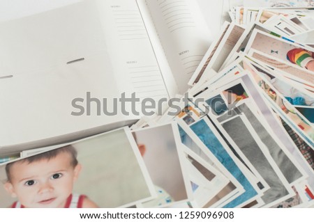 Pile of printed photographs in disorder on a white background near a photoalbum. Picture of the baby on the top.