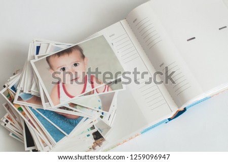 Pile of printed photographs in disorder and a photoalbum on a white background. Picture of the baby on the top.