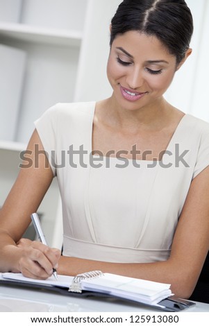 Beautiful young mixed race, Latina Hispanic woman or businesswoman in smart business suit sitting at a desk in an office writing in her diary