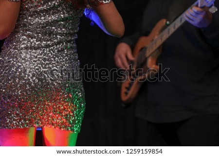Singer in a silver dress dancing with a guitarist in he background. 
