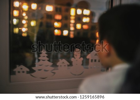 The little boy will overcome in a window. Outside the window lamps burn. The lonely child celebrates Christmas. The orphan in orphanage Royalty-Free Stock Photo #1259165896