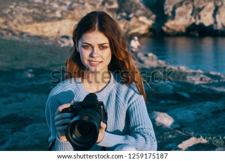 Beautiful woman holds in her hand a camera in the mountains near the sea                        