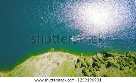 The boat floats on the lake, top view. Shooting with the drone. Beautiful view of the lake in the gorge. Around coniferous trees, firs grow. Green hills in the grass. Blue and green water of the lake.