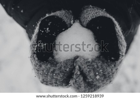 Woman in gray gloves holds snow in hands in shape of heart.
