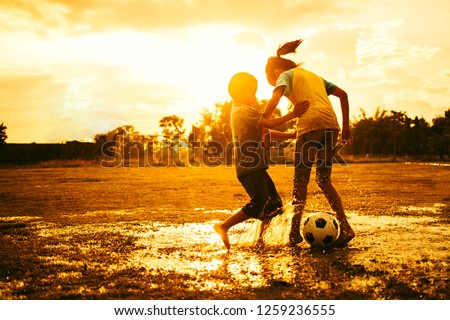 An action sport picture of a group of kids playing soccer football for exercise in community rural area under the sunset.
