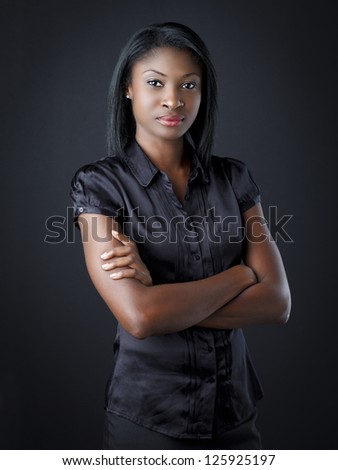 Portrait of a smart young businesswoman with arms folded over black background