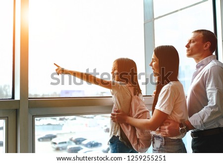 Family at the airport, waiting for their flight. They look near the window, my daughter shows her finger on the plane. Everyone looks out the window