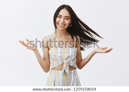 Carefree attractive girlfriend walking on seashore with boyfriend on windy weather, hair floats on wind and woman feeling happy, gazing at camera joyfully, lifting hands up as if she is goddess