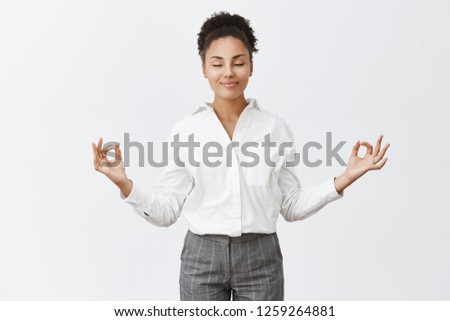 Stress free, only peace inside. Charming relaxed and carefree female in bossy outfit, raising hands in zen gesture, smiling with closed eyes while meditating or practicing yoga, feeling relieved