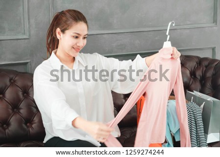 Beautiful asian women wore white shirt ,holding shopping bag,Pink shirt in hand,looking laptop in gray living room ,working private business at home 
