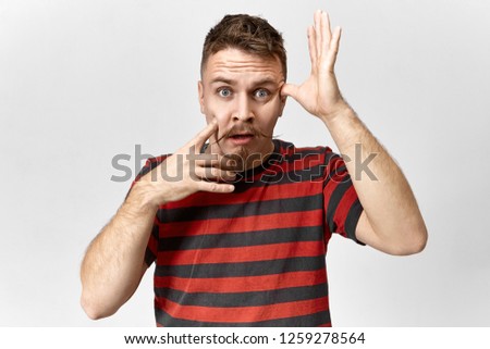 Picture of attractive young man with handlebar mustache and goatee beard having forgotful panic look, looking at camera with opened mouth, forgot to do something very important. Human feelings