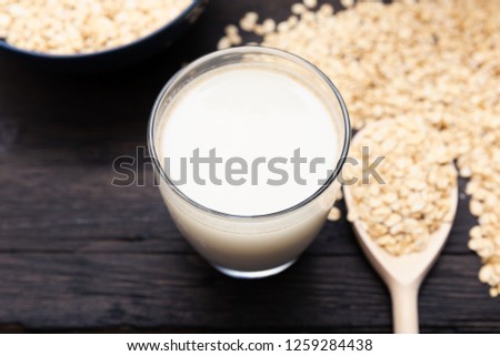 Glass of vegan, dairy-free oat milk and oats on a dark wooden background with texture. Concept of a vegan diet.