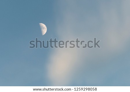 Half moon in the sky with white clouds floating through.