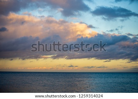 blue sky white clouds over calm body of water in summer with green foliage, trees and grass on the shores