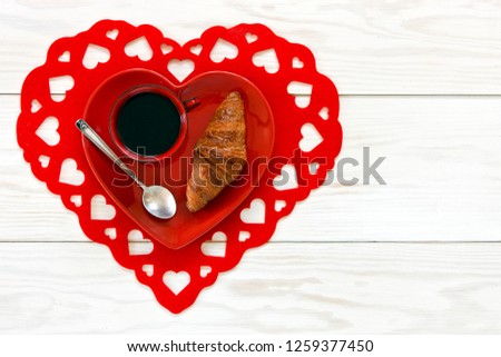 Red Cup of black tea and fresh homemade croissant on red heart shape plate.  Close up, top view on white wooden background