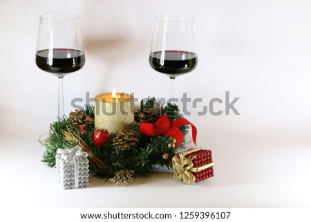 Two glasses of red wine, a burning golden candle, a wreath on a white background.