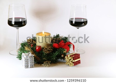 Two glasses of red wine, a burning golden candle, a wreath on a white background.
