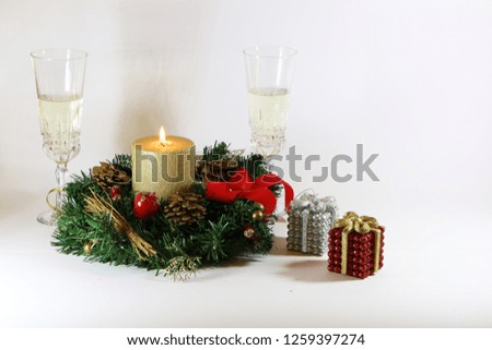 Two glasses of champagne, a burning golden candle, a wreath on a white background.