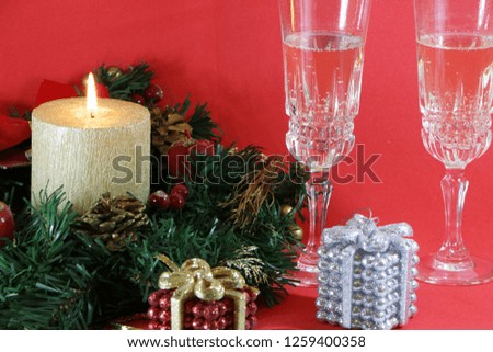 Two glasses of champagne, a burning golden candle, a wreath on a red background