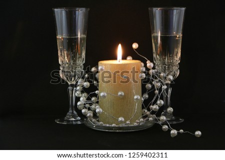 Two glasses of champagne, a burning red candle, a wreath on a white background.