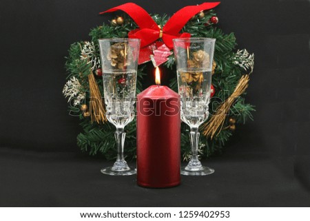 Two glasses of champagne, a burning red candle, a wreath on a black background