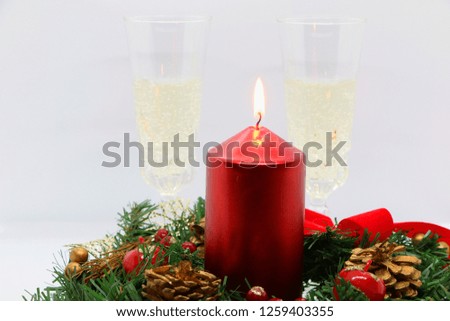 Two glasses of champagne, a burning red candle, a wreath on a white background.