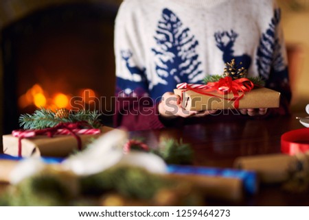 Beautiful gift in the hands of men. New Year's gift with a red ribbon, fir on the table. The man made it himself and is going to give for the holiday. Beautiful background with fireplace. 