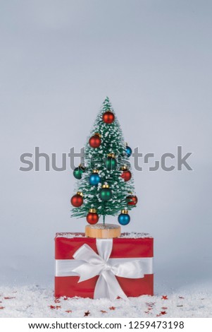 Little Christmas tree with ornaments on little gift pack with snow and shining little stars