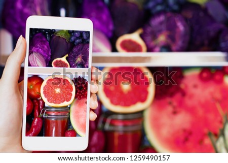 Vegan vegetarian woman female taking picture of healthy antioxidant colorful food, veggies, raw juice and fruits for eating in fridge: grapefruit, tomatoes, watermelon, fig and onion by smartphone