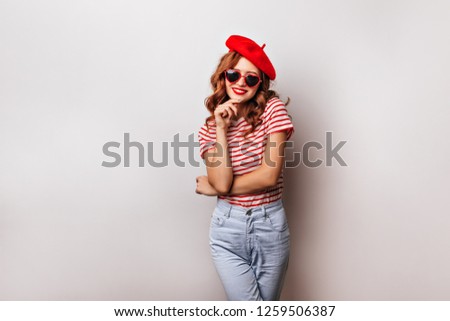 Happy french girl in jeans expressing positive emotions. Spectacular female model in beret and sunglasses smiling on white background.