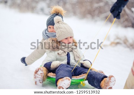 Little adorable girls sledding and playing outdoors in snow. Family vacation on Christmas eve outdoors