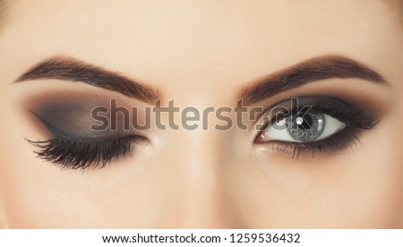 Beautiful woman with long eyelashes and with beautiful evening make-up. Eyes close up. One eye is closed and the other is open.  Royalty-Free Stock Photo #1259536432