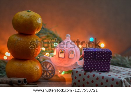 A snowman of three mandarins, a Cinderella carriage, a branch of spruce, christmas lights, boxes of gifts. Christmas fabulous picture. Good New Year spirit. 